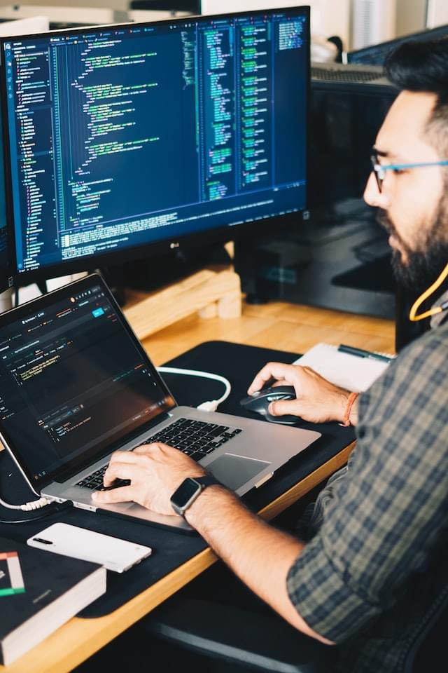 Image of a man in front of two screens reading code files