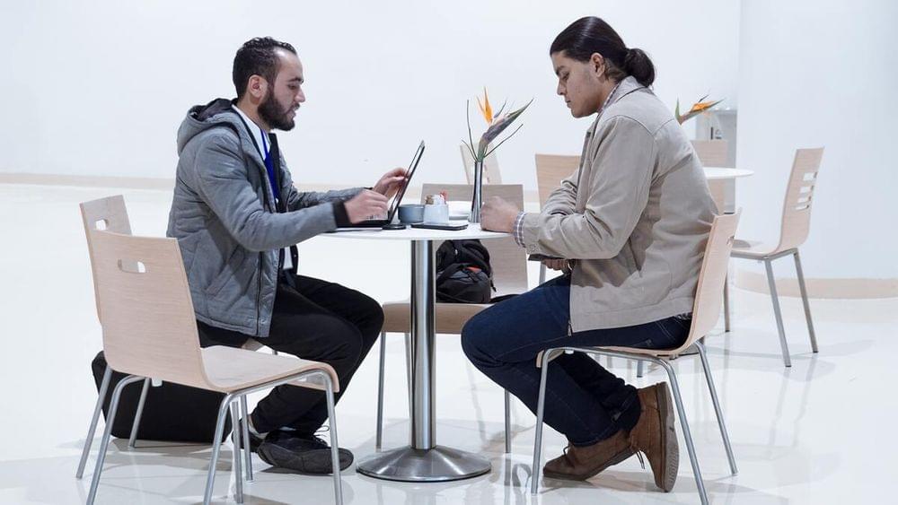 Sitting man using laptop near woman sitting beside table